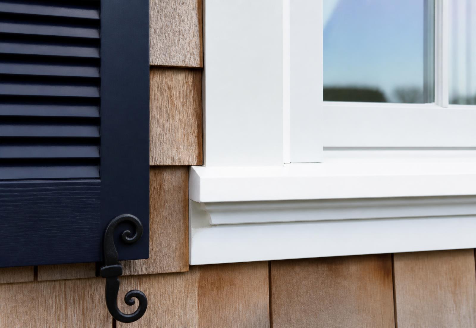 Close-up of crisp white exterior trim against cedar shingle siding with a navy shutter on a coastal New England home